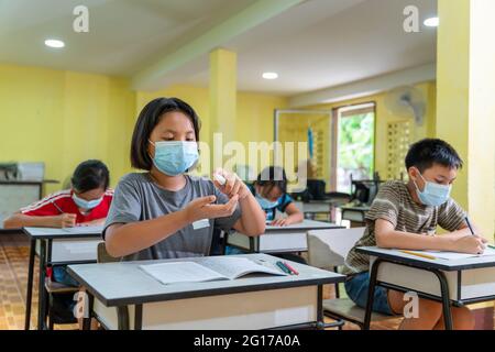 Les enfants asiatiques dans la salle de classe portent un masque facial et utilisent un antiseptique pour la prévention du coronavirus. Les écoles primaires sont prêtes à étudier après Covid-19 Banque D'Images