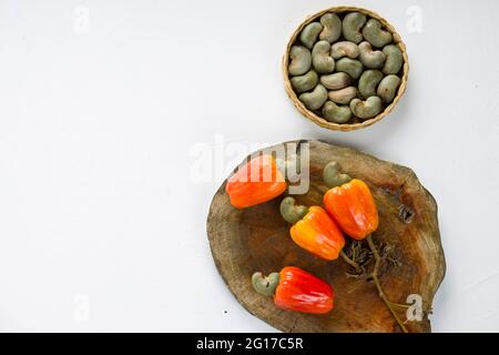 Pomme de noix de cajou et graines de noix de cajou disposées sur un morceau de bois qui est placé sur fond blanc, foyer sélectif et vue de dessus. Banque D'Images