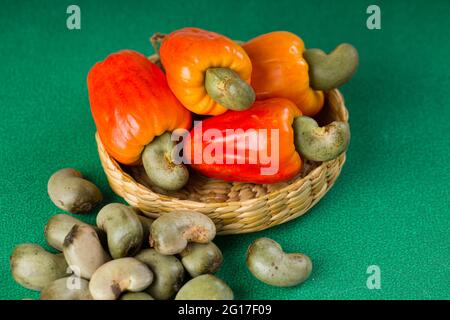 Pomme de noix de cajou et graines de noix de cajou disposées dans un panier placé sur un fond vert texturé Banque D'Images