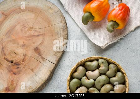 Pomme de noix de cajou et graines de noix de cajou disposées sur un fond texturé gris avec un morceau de bois placé à proximité, vue du dessus. Banque D'Images