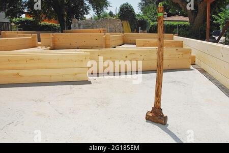 Un vieux marteau en bois sur les fondations d'une maison en bois partiellement construite (en sapin), une maison en bois prédécoupée qui est assemblée sur place Banque D'Images