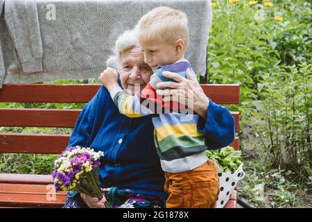 femme âgée de 90 ans grande-grand-mère embrassant grand-petit-fils. Enfant garçon soutenant et donnant des fleurs à la grande-grand-mère. Groupe de famille, soutien Banque D'Images