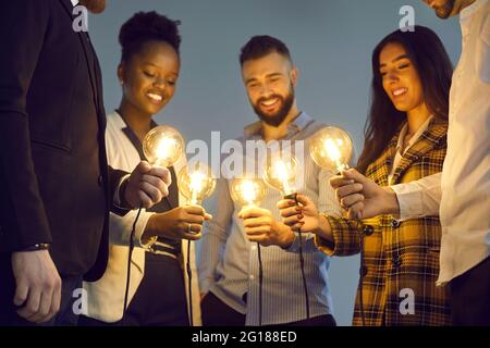 Une équipe d'affaires diversifiée se joint aux ampoules brillantes pour partager des idées créatives Banque D'Images