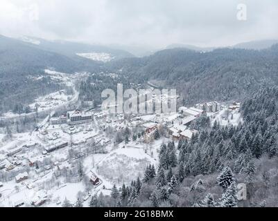 Vue aérienne d'un village de montagne avec des collines couvertes de neige et de forêt de pins en hiver. Yaremche, Ukraine. Survolant les collines enneigées et le bois Banque D'Images
