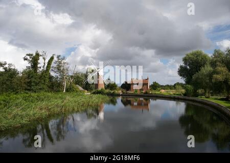 Un moulin à vent traditionnel (pompe à vent) et joli chalet sur un virage dans une rivière dans les Norfolk Broads, Angleterre, Royaume-Uni. Réflexion parfaite sous le spectaculaire sto Banque D'Images