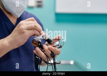 Crop ophtalmologiste anonyme dans masque respiratoire mesurant la puissance optique de la lentille de lunettes avec diopter à l'hôpital Banque D'Images