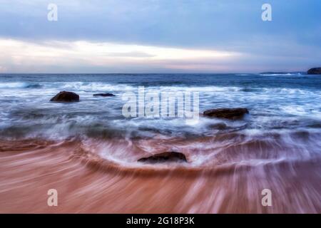 Pierres de roche au large de la plage de Mona Vale en surf à marée haute au lever du soleil - Sydney pacific Coast Seascape. Banque D'Images