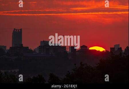 Wimbledon, Londres, Royaume-Uni. 6 juin 2021. Disque orange du soleil se levant au-dessus des toits distants de Londres. Le grand bâtiment avec trois éoliennes sur le toit est Strata SE1, une tour résidentielle de 43 étages à Elephant & Castle. Crédit : Malcolm Park/Alay Live News Banque D'Images