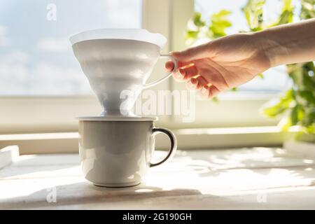 La main d'une femme retire un entonnoir avec un filtre de la tasse. Autre mode de préparation du café. Filtre V60 avec café moulu. Vue latérale. Banque D'Images