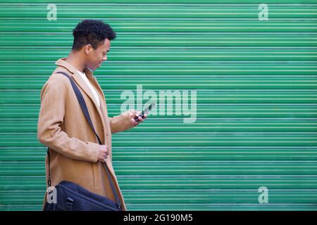 Jeune homme noir utilisant un smartphone près d'un mur urbain. Banque D'Images