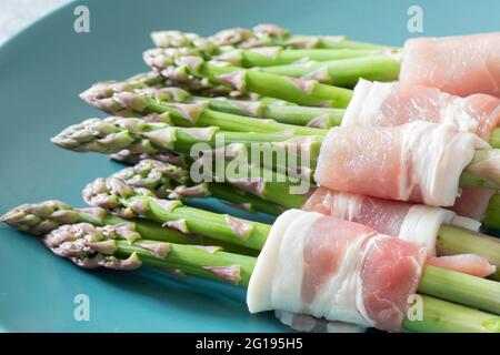 Asperges enrobées de bacon sur une assiette verte bleue. Avec un arrière-plan concret Banque D'Images