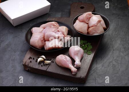 Ensemble de coupes de poulet cru, combinaison de coupes de curry de poulet sans peau, de coupes de poulet et de deux pilons disposés sur une planche en bois avec des feuilles de coriandre Banque D'Images