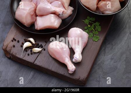 Ensemble de coupes de poulet cru, combinaison de coupes de curry de poulet sans peau, de coupes de poulet et de deux pilons disposés sur une planche en bois avec des feuilles de coriandre Banque D'Images