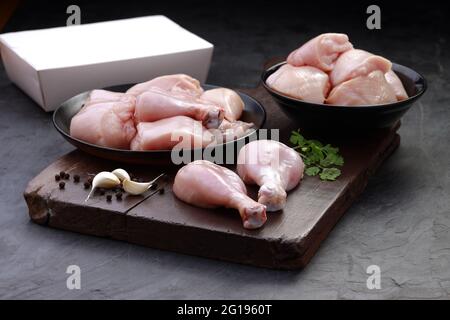 Ensemble de coupes de poulet cru, combinaison de coupes de curry de poulet sans peau, de coupes de poulet et de deux pilons disposés sur une planche en bois avec des feuilles de coriandre Banque D'Images