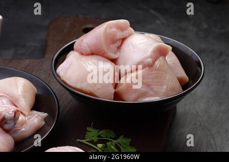 Ensemble de coupes de poulet cru, combinaison de coupes de curry de poulet sans peau, de coupes de poulet et de deux pilons disposés sur une planche en bois avec des feuilles de coriandre Banque D'Images