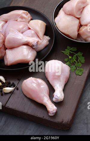 Ensemble de coupes de poulet cru, combinaison de coupes de curry de poulet sans peau, de coupes de poulet et de deux pilons disposés sur une planche en bois avec des feuilles de coriandre Banque D'Images