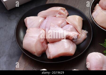 Ensemble de coupes de poulet cru, combinaison de coupes de curry de poulet sans peau, de coupes de poulet et de deux pilons disposés sur une planche en bois avec des feuilles de coriandre Banque D'Images