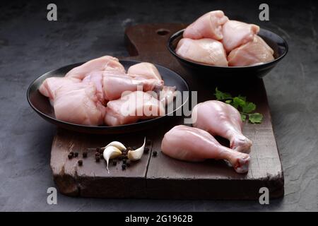 Ensemble de coupes de poulet cru, combinaison de coupes de curry de poulet sans peau, de coupes de poulet et de deux pilons disposés sur une planche en bois avec des feuilles de coriandre Banque D'Images