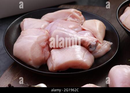 Ensemble de coupes de poulet cru, combinaison de coupes de curry de poulet sans peau, de coupes de poulet et de deux pilons disposés sur une planche en bois avec des feuilles de coriandre Banque D'Images