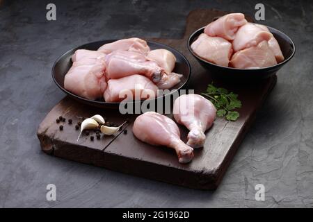 Ensemble de coupes de poulet cru, combinaison de coupes de curry de poulet sans peau, de coupes de poulet et de deux pilons disposés sur une planche en bois avec des feuilles de coriandre Banque D'Images