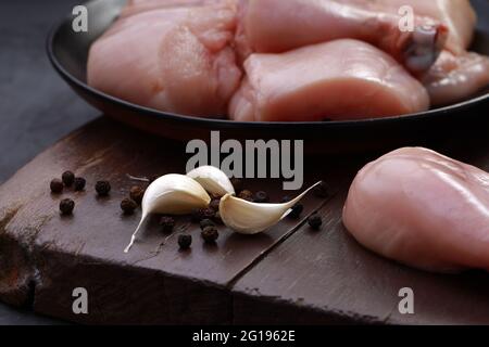 Ensemble de coupes de poulet cru, combinaison de coupes de curry de poulet sans peau, de coupes de poulet et de deux pilons disposés sur une planche en bois avec des feuilles de coriandre Banque D'Images