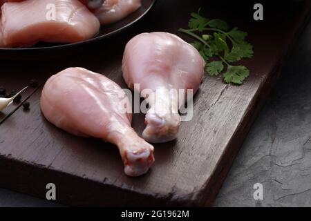 Ensemble de coupes de poulet cru, combinaison de coupes de curry de poulet sans peau, de coupes de poulet et de deux pilons disposés sur une planche en bois avec des feuilles de coriandre Banque D'Images