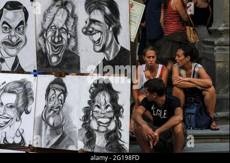 Des stars du cinéma, de la télévision et de la pop telles que Tom Cruise, Julia Roberts, Rowan Atkinson et Michael Jackson, caricaturées par l'un des artistes de rue autorisés offrant des portraits rapides à l'extérieur de la Galerie des Offices à Florence, en Toscane, en Italie, Contrastant avec les touristes qui regardent le monde passer des marches de la galerie à Piazzale degli Uffizi tout en prenant une pause de tourisme. Banque D'Images