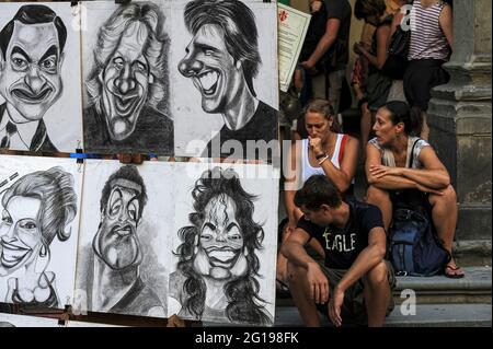 Des stars du cinéma, de la télévision et de la pop telles que Tom Cruise, Julia Roberts, Rowan Atkinson et Michael Jackson, caricaturées par l'un des artistes de rue autorisés offrant des portraits rapides à l'extérieur de la Galerie des Offices à Florence, en Toscane, en Italie, Contrastant avec les touristes qui regardent le monde passer des marches de la galerie à Piazzale degli Uffizi tout en prenant une pause de tourisme. Banque D'Images