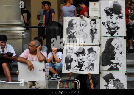 Des stars de cinéma de l'âge d'or d'Hollywood telles que Charlie Chaplin, Marilyn Monroe, Marlene Dietrich et Bette Davis, caricaturées par l'un des artistes de rue autorisés offrant des portraits rapides à l'extérieur de la Galerie des Offices, à Florence, en Toscane, en Italie, Contrastant avec les touristes qui grince et regardent le monde passer des marches de la galerie à Piazzale degli Uffizi. Banque D'Images