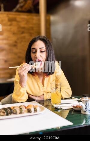 Une jeune femme hispanique mange des sushis dans un restaurant japonais. Dîner de style de vie pour des amis indépendants et confiants prenant des aliments sains. Jaune Banque D'Images