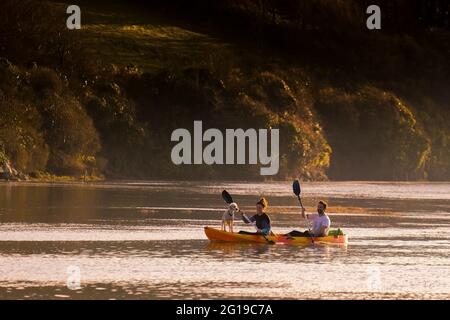 Les kayakistes et leur chien pagayer sur la rivière Gannel lors d'un séjour de vacances de détente alors que le soleil se couche à Newquay, dans les Cornouailles. Banque D'Images