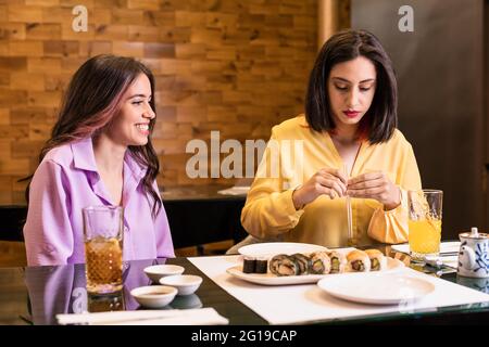Une jeune femme hispanique mange des sushis dans un restaurant japonais. Style de vie dîner amis prendre des aliments sains. Jaune et lavande couleur 2021 ans Banque D'Images
