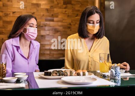 Une jeune femme hispanique mange des sushis dans un restaurant japonais. Style de vie nouveau dîner normal portant masque pour les amis covid . Jaune et lavande Banque D'Images