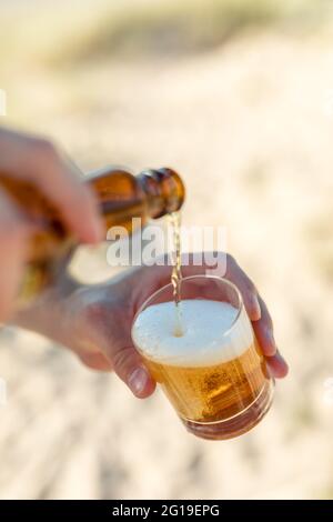 Homme versant de la bière lager dans un verre à la plage Banque D'Images