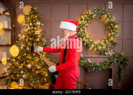 Le Père Noël à la maison lit une lettre et une liste de souhaits pour enfants. Sapin de Noël décoré avec des lumières. Cadeaux, surprise pour le nouvel an Banque D'Images