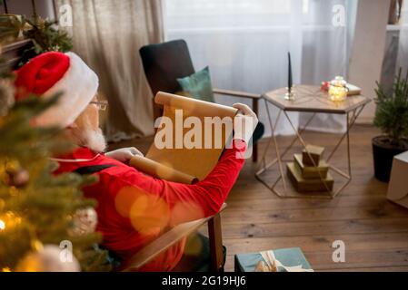 Le Père Noël à la maison lit une lettre et une liste de souhaits pour enfants. Sapin de Noël décoré avec des lumières. Cadeaux, surprise pour le nouvel an Banque D'Images