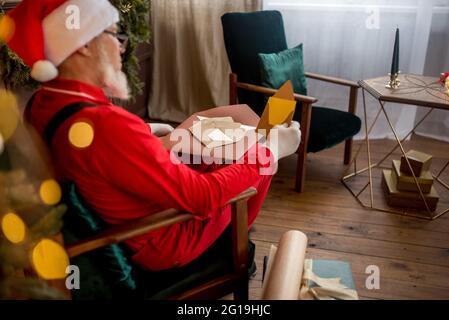 le père Noël moderne de luxe à la maison lit une lettre et une liste de souhaits pour les enfants. Arbre de Noël joliment décoré avec des cadeaux de lumière et surprise pour New Yea Banque D'Images