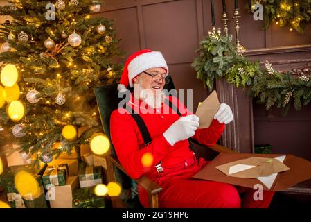 le père Noël moderne de luxe à la maison lit une lettre et une liste de souhaits pour les enfants. Arbre de Noël joliment décoré avec des cadeaux de lumière et surprise pour New Yea Banque D'Images