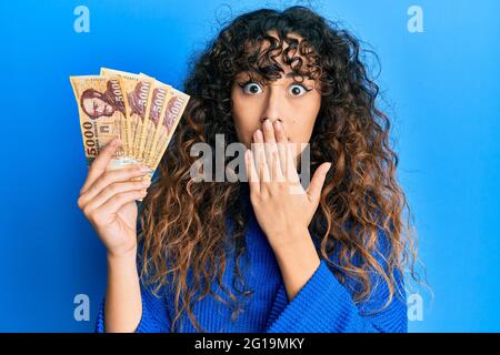 Jeune fille hispanique détenant 5000 billets de forint hongrois couvrant la bouche avec la main, choquée et effrayée pour erreur. Expression surprise Banque D'Images