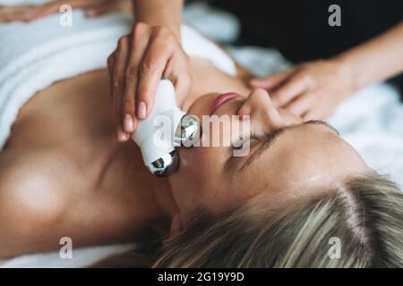 La jeune femme blonde bénéficie d'un massage du visage avec un masseur pour le visage microcurrent au spa, faites-vous plaisir. Soins du corps professionnels Banque D'Images