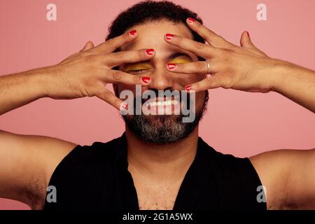 Homme liquide de genre montrant son maquillage et souriant. Homme heureux portant vernis à ongles et maquillage pour les yeux. Banque D'Images