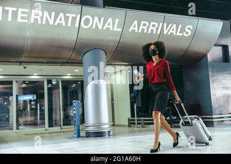 Femme d'affaires portant un masque facial avec des bagages marchant dans le terminal de l'aéroport. Un voyageur international est arrivé avec une valise pendant une pandémie. Banque D'Images