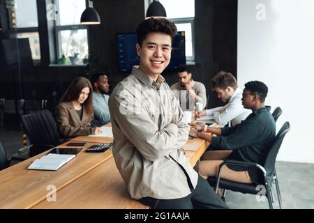 Un jeune homme d'affaires asiatique assis sur son bureau et posant Banque D'Images