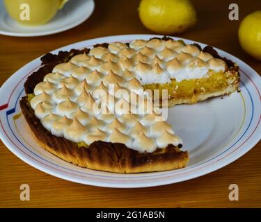 Tarte au citron avec merengue sans une tranche dans un plat décoré de deux citrons et d'une tasse de café Banque D'Images