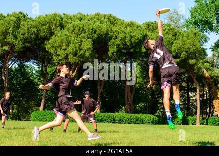 Groupe de jeunes adolescents en équipe jouant à un jeu de Frisbee dans les portes d'entrée du parc. L'homme sautant attrape un Frisbee à un coéquipier dans un Frisbee ultime Banque D'Images