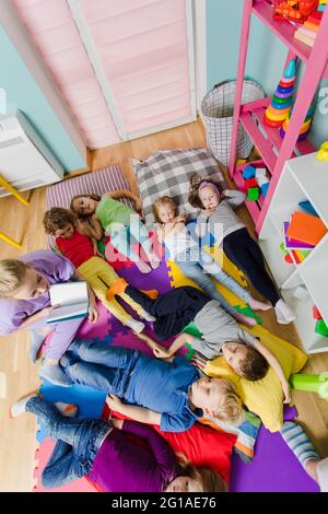 Les enfants actifs s'assetent sur des oreillers et des tapis moelleux à la maternelle Banque D'Images