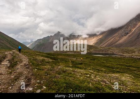 Les touristes marchent le long de la vallée le long du chemin des pierres dans les montagnes par temps sombre. Un petit lac. Chaînes de montagnes hautes et nuages bas. Horizon Banque D'Images