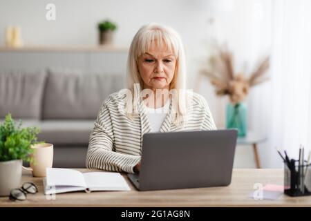 Femme mûre concentrée assise sur un bureau et travaillant sur un ordinateur Banque D'Images