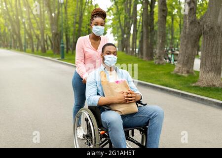 Une jeune femme et son petit ami handicapé en fauteuil roulant portant des masques faciaux, marchant dans le parc pendant le covid Banque D'Images