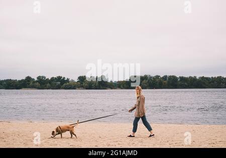 Une femme marche son chien le long de la rive de la rivière sur une plage de sable par temps sombre Banque D'Images